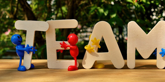 Holzbuchstaben "Team", davor und daneben bunte Figuren